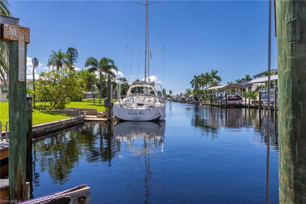 Waterfront property featuring a private boat dock, lush green lawn, and mature palm trees