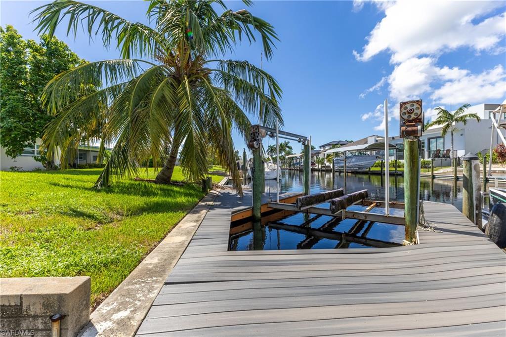 Waterfront property featuring a composite dock, boat lift, direct canal access, and lush green lawn with a mature palm tree