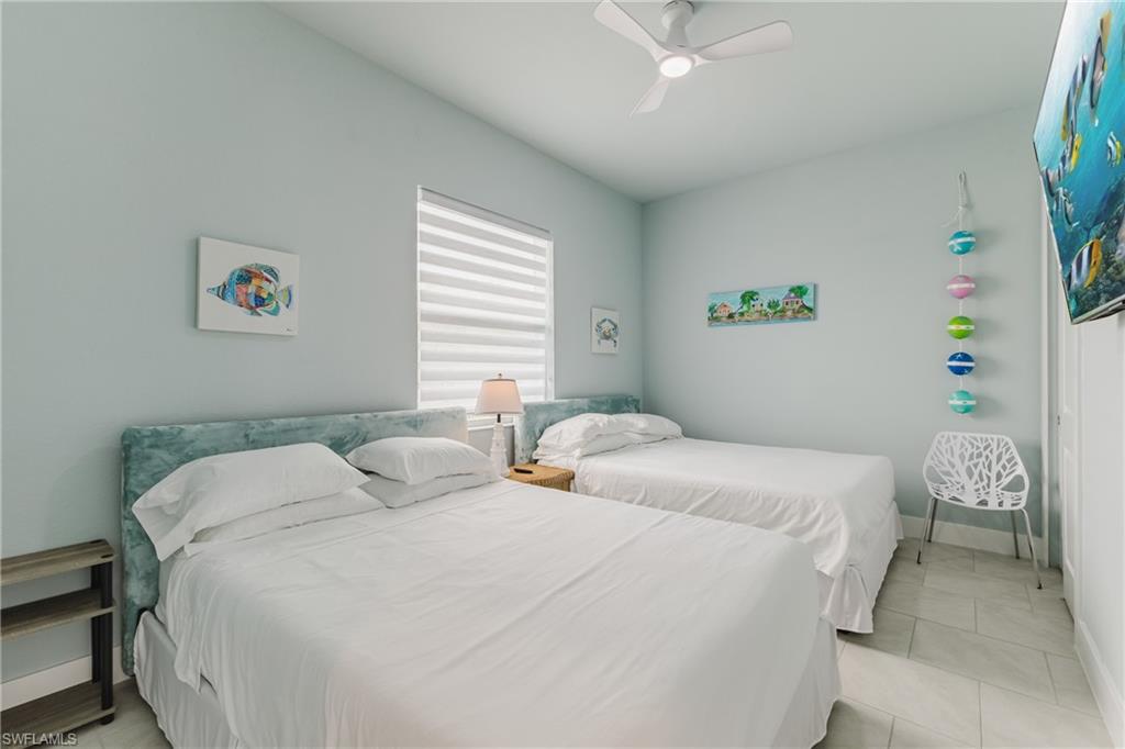 Bedroom featuring two beds with upholstered headboards, a ceiling fan, and tiled flooring