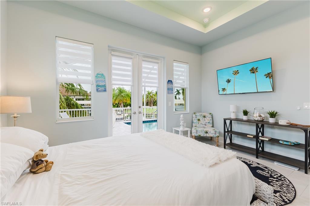 Light-filled bedroom featuring direct patio access, tray ceiling with recessed lighting, and expansive windows