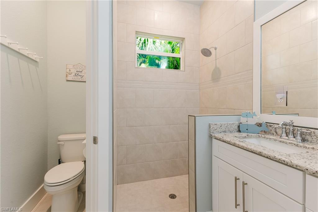 Bathroom featuring a walk-in shower with tile surround and rain shower head, white vanity with granite-look countertop, integrated sink, and chrome fixtures