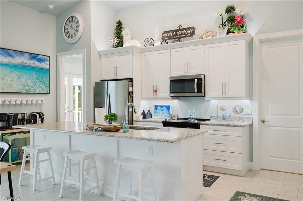 White cabinetry kitchen featuring a built-in microwave, stainless steel refrigerator, and a spacious island with bar seating