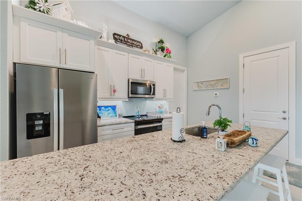 Spacious kitchen island featuring a granite-finish countertop, stainless steel appliances, white shaker-style cabinetry, and a modern gooseneck faucet