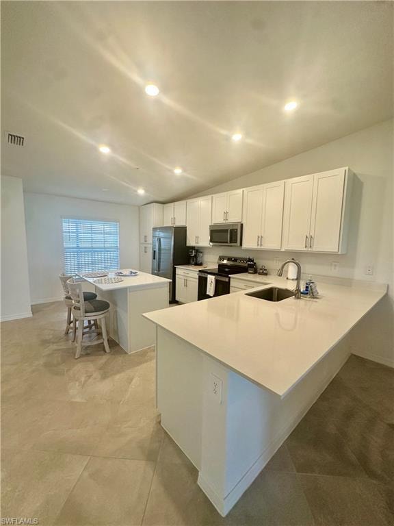 Kitchen featuring a sink, stainless steel appliances, light countertops, a breakfast bar area, and white cabinets