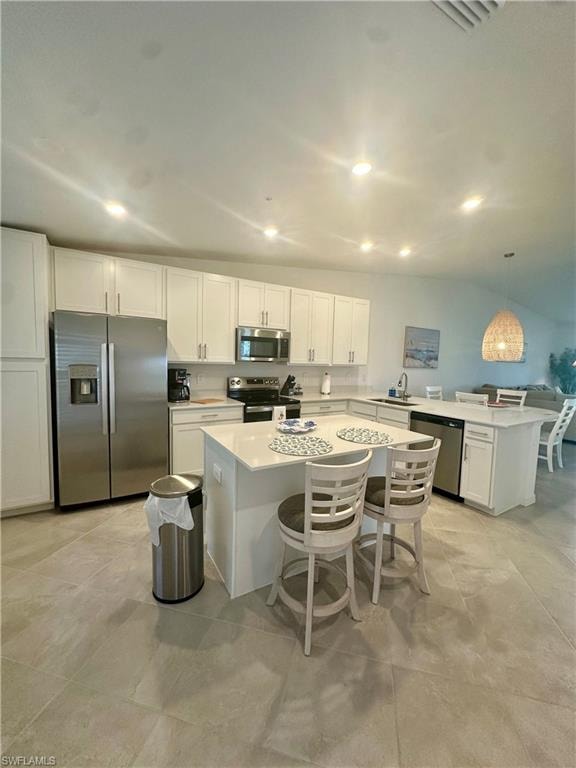 Kitchen featuring appliances with stainless steel finishes, a kitchen bar, white cabinetry, light countertops, and recessed lighting