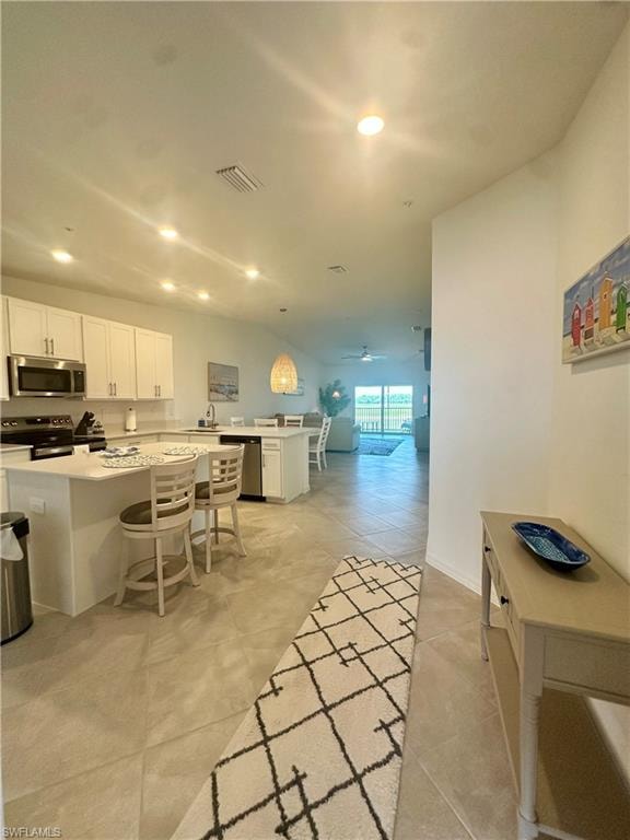 Kitchen with stainless steel appliances, a kitchen breakfast bar, light countertops, white cabinets, and a ceiling fan