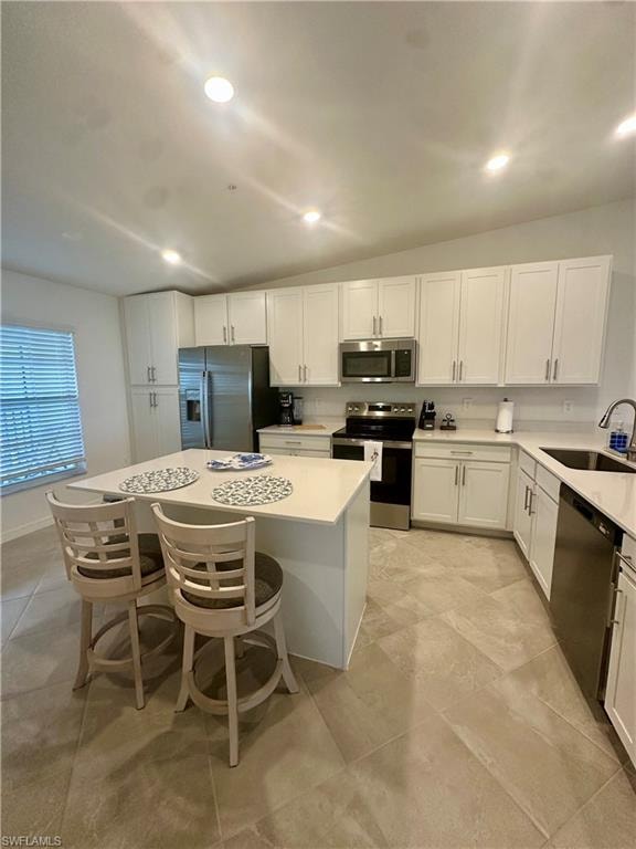 Kitchen with stainless steel appliances, a sink, white cabinets, a kitchen island, and light countertops