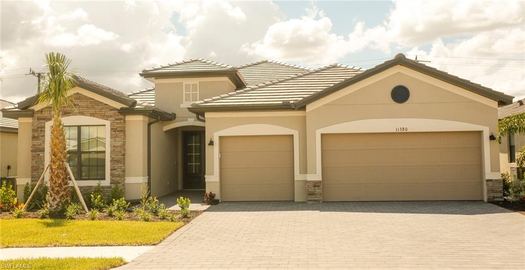 Contemporary stucco exterior featuring stone accents, a tile roof, an arched entry, a palm tree, and a paver driveway