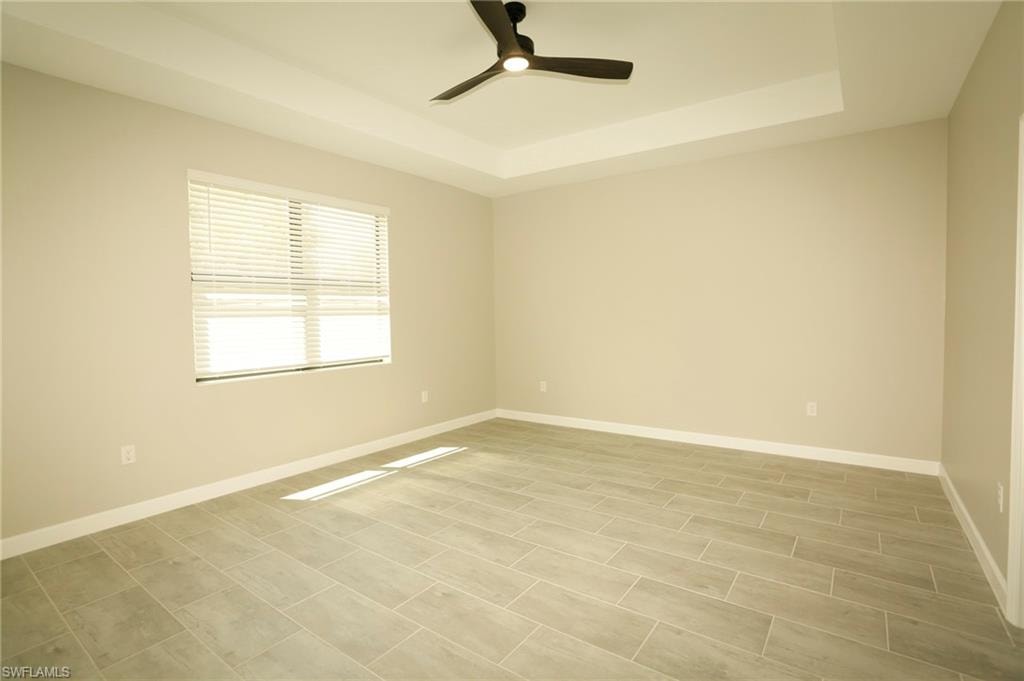 Spacious room featuring a tray ceiling with a ceiling fan, light wood-finish plank tile flooring, and a large window with horizontal blinds