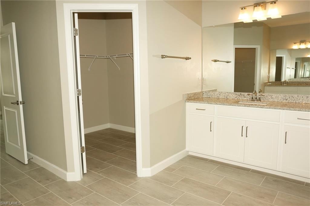Bathroom featuring a double vanity with granite countertop, white cabinetry, and brushed nickel hardware
