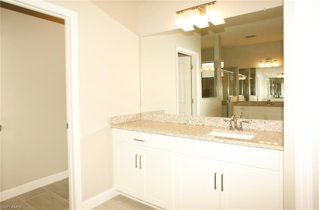 Bathroom vanity featuring a light-colored granite countertop, an undermount sink with a chrome faucet, and white cabinetry
