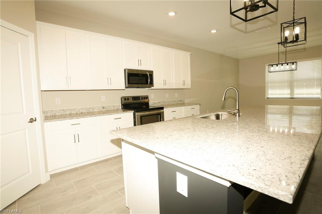 Kitchen featuring a large island with sink, ample white cabinetry, stainless steel appliances, speckled countertops, and wood-finish tile flooring