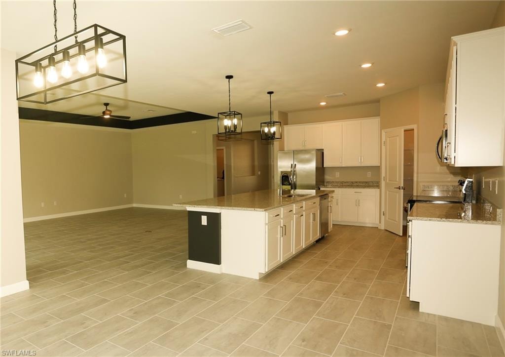 Kitchen and living area featuring a large center island, white cabinetry, stainless steel appliances, and tile flooring