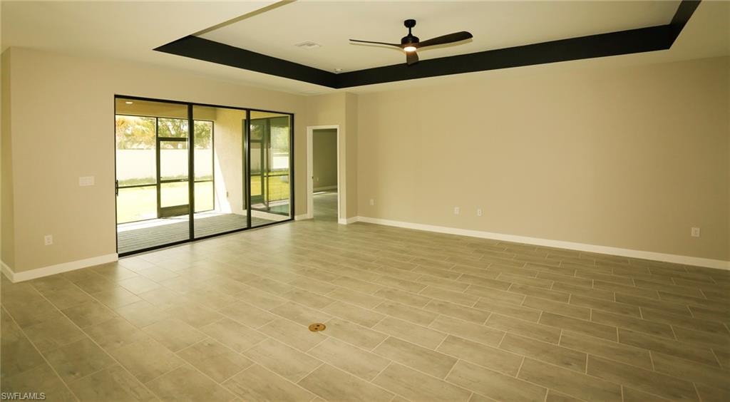 Spacious interior featuring wood-finish tile flooring, a tray ceiling with a dark accent, and a ceiling fan