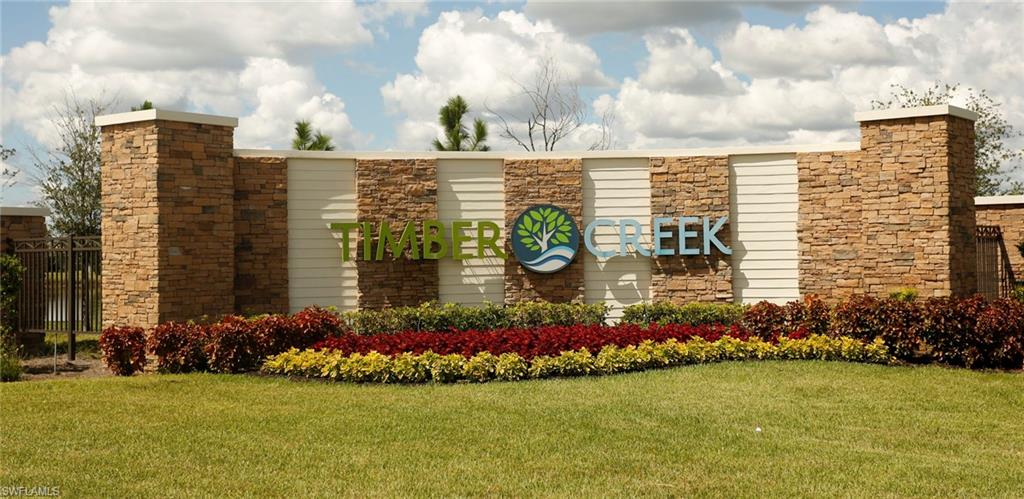 Stone and siding community entrance sign featuring a decorative metal gate