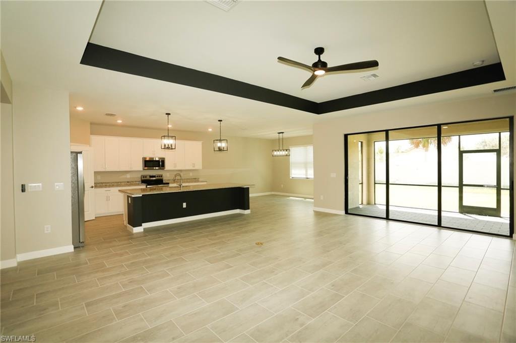 Open-concept living area featuring light-toned tile flooring, a tray ceiling with a dark accent, and a modern ceiling fan