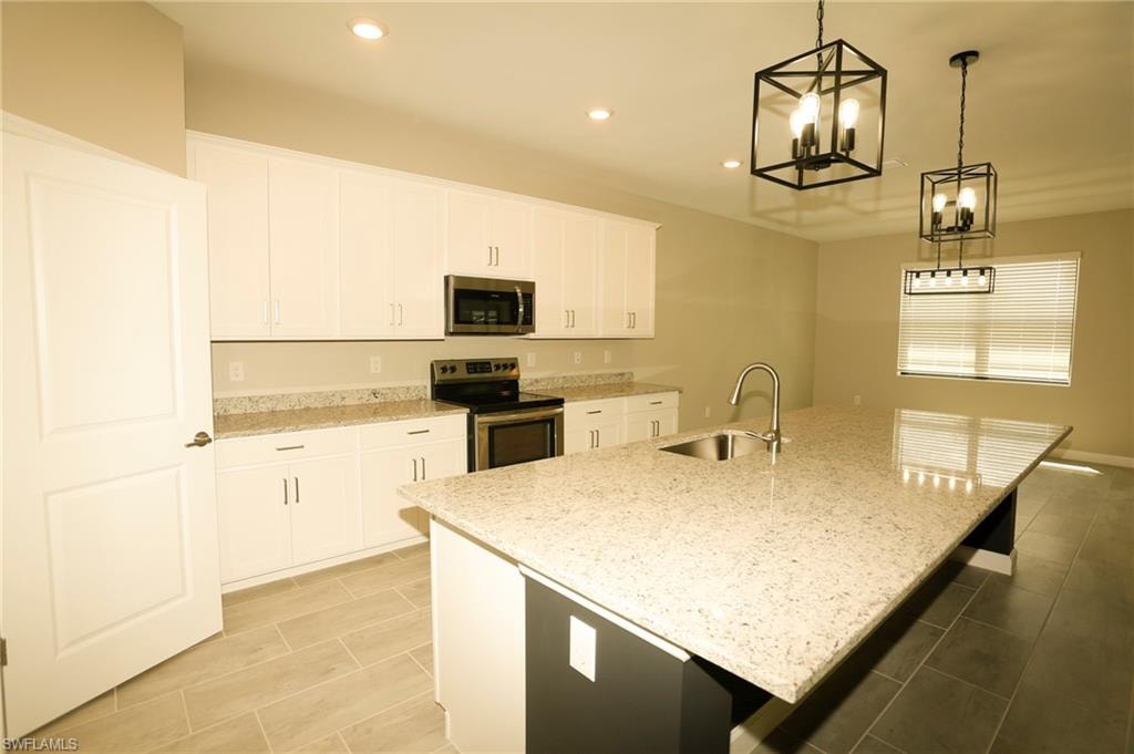 Spacious kitchen featuring an expansive island with an undermount sink, white cabinetry, integrated stainless steel appliances, and tile flooring