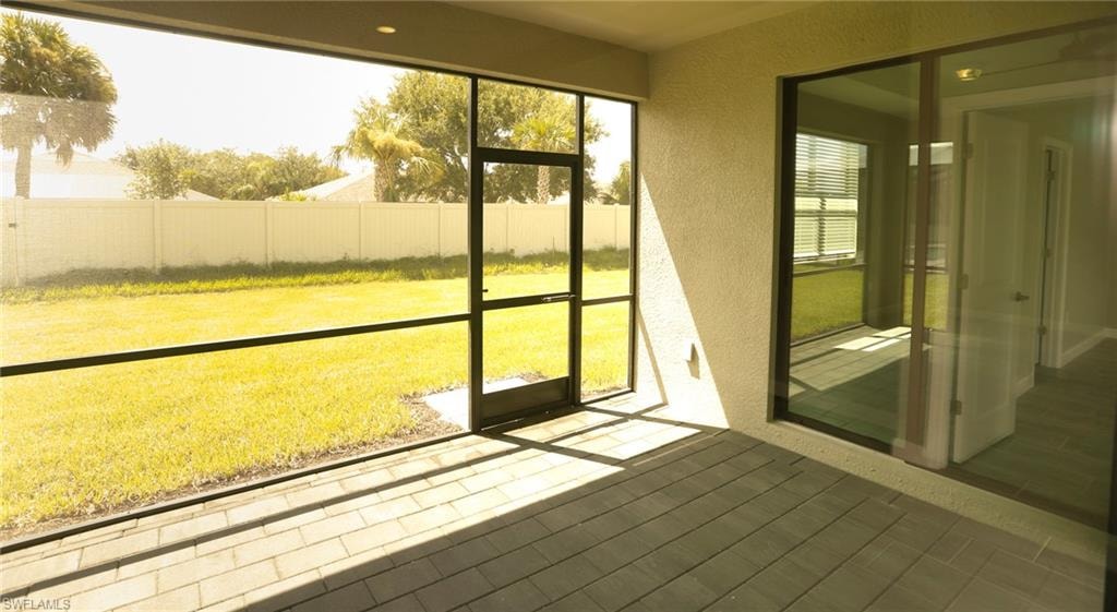 Screened lanai featuring paver flooring, direct patio access, and an expansive lawn beyond a privacy fence