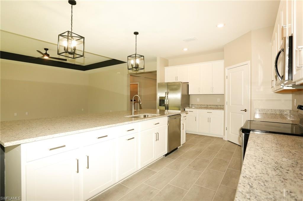 Open-concept kitchen featuring an oversized island with an undermount sink, pendant lighting, stainless steel appliances, white cabinetry, and granite countertops