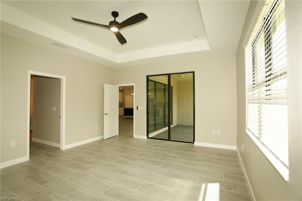 Spacious room featuring light gray wall paint, tray ceiling with a modern ceiling fan, and large format tile flooring