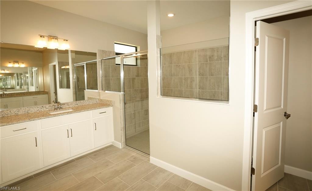 Bathroom featuring a double vanity with stone countertops, a large frameless mirror, and a spacious glass-enclosed shower with tiled walls