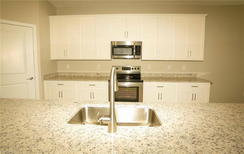 Spacious kitchen featuring an undermount stainless steel sink, brushed nickel faucet, and a large granite countertop island