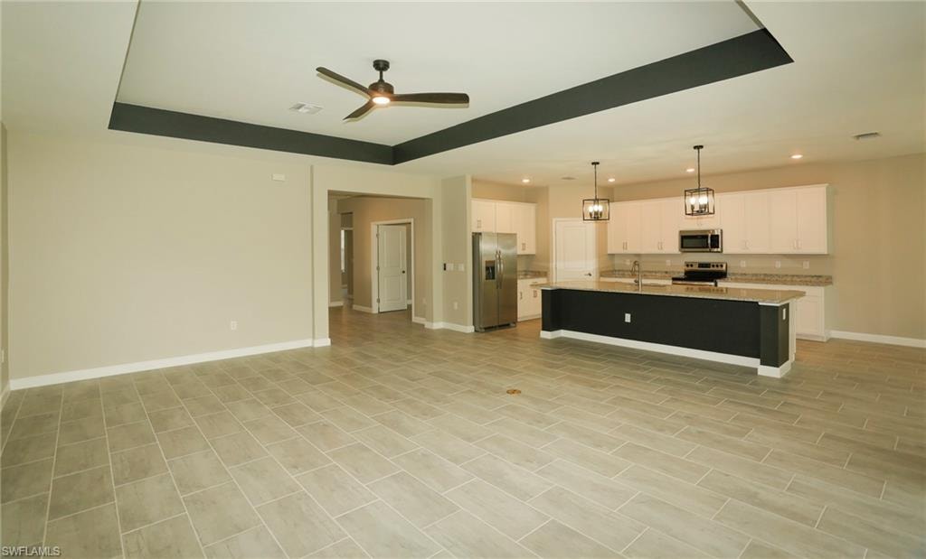 Open-concept living space featuring wood-finish tile flooring, a tray ceiling with a ceiling fan, and recessed lighting