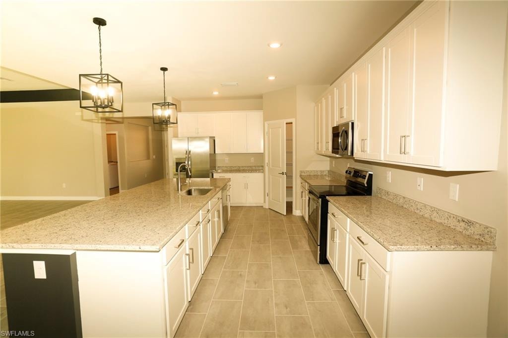 Open-concept kitchen featuring an oversized island with an undermount sink, white cabinetry, granite countertops, and stainless steel appliances