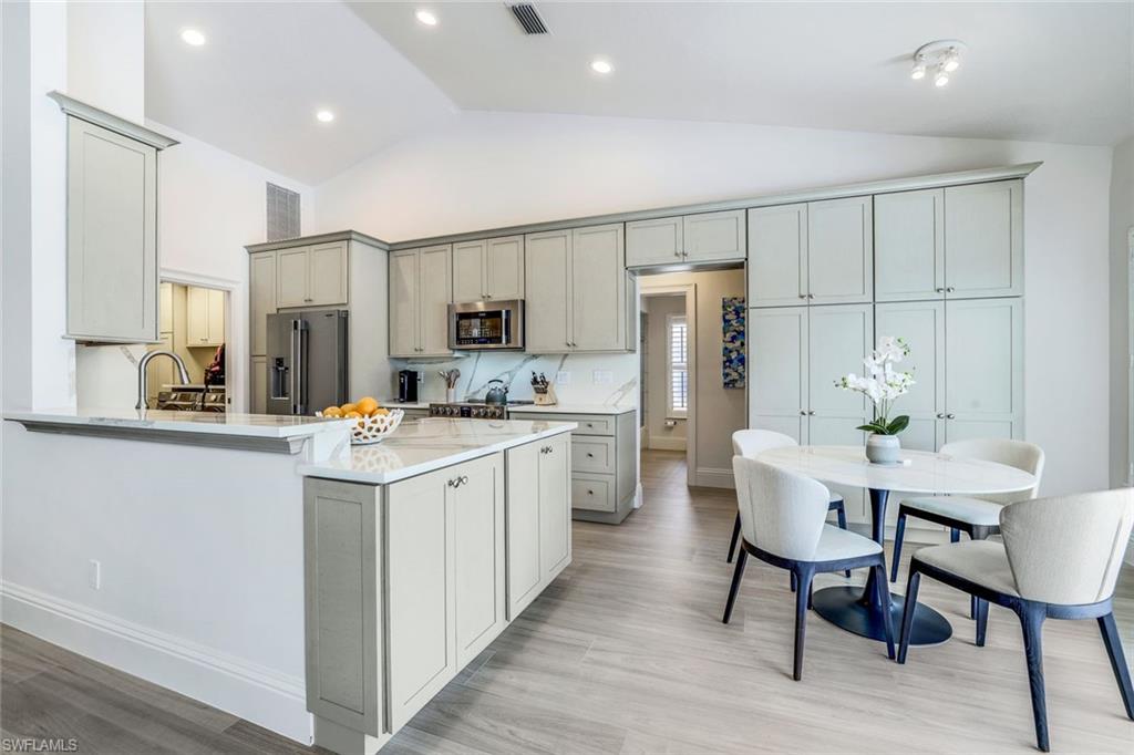 Kitchen with gray cabinetry, light hardwood / wood-style flooring, appliances with stainless steel finishes, kitchen peninsula, and high vaulted ceiling
