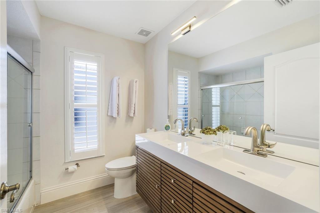 Full bathroom with double sink vanity, shower / bath combination with glass door, toilet, and wood-type flooring