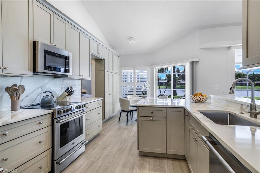 Kitchen with light wood-type flooring, backsplash, sink, lofted ceiling, and appliances with stainless steel finishes
