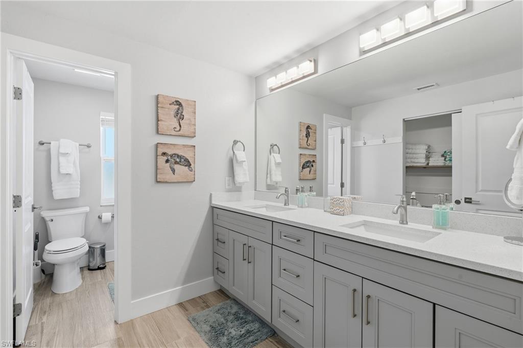 Dual vanity with gray shaker cabinetry, integrated sinks, and light-toned countertops - Virtually Edited Image