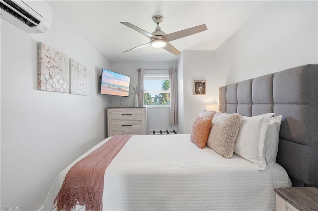 Bedroom featuring a padded fabric headboard, wall-mounted television, and a window with natural light - Virtually Edited Image