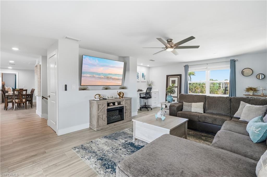 Open concept living area featuring wood-finish flooring, recessed lighting, a modern ceiling fan, large windows, and a built-in media console - Virtually Edited Image
