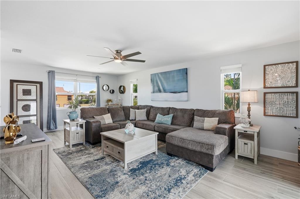 Spacious living area featuring light wood-finish flooring, recessed lighting, and a contemporary ceiling fan - Virtually Edited Image