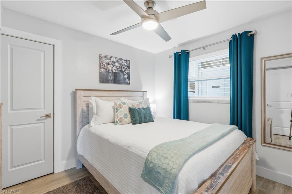Bedroom featuring light wood-finish flooring, a contemporary ceiling fan, and a paneled interior door - Virtually Edited Image