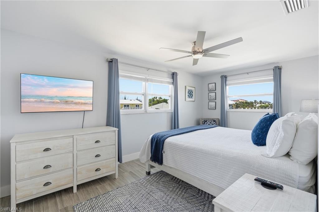 Bright room featuring multiple windows with blue drapes, a ceiling fan with light, and wood-finish flooring - Virtually Edited Image