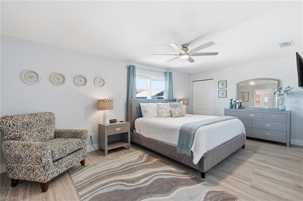 Spacious bedroom featuring wood-finish flooring, a contemporary ceiling fan, window with light-filtering curtains, and a built-in closet with bi-fold doors - Virtually Edited Image
