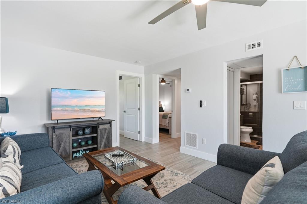 Open-concept living area featuring light wood-finish flooring, a contemporary ceiling fan, and crisp white walls - Virtually Edited Image