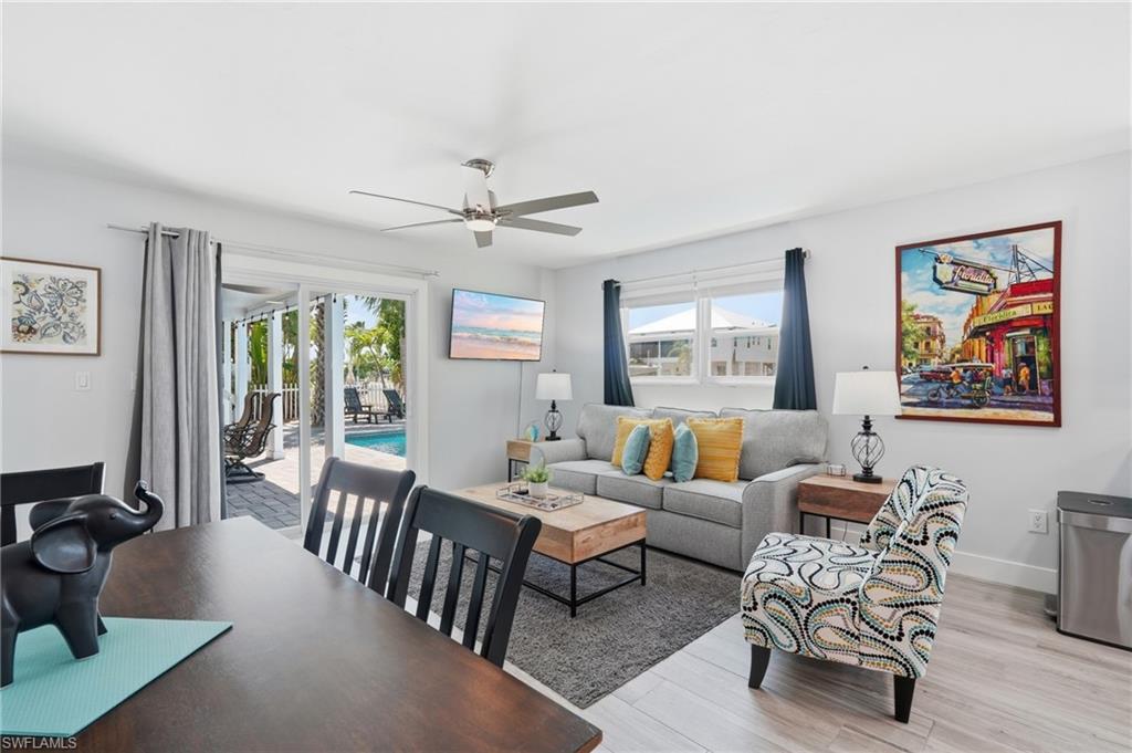 Open-concept living space featuring wood-finish flooring, a contemporary ceiling fan, and sliding glass doors opening to an exterior patio with a swimming pool - Virtually Edited Image