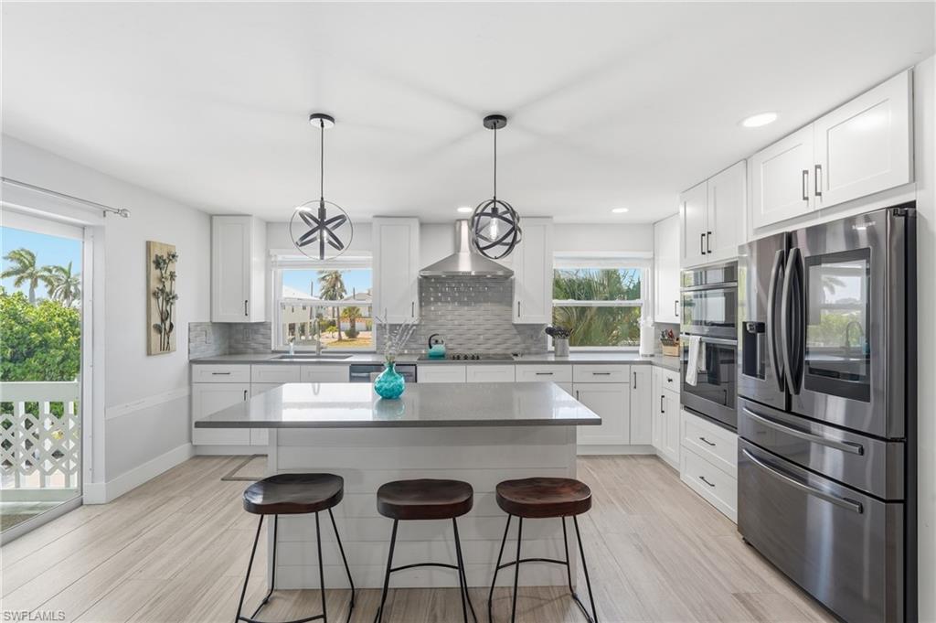 Modern kitchen featuring white shaker cabinetry, stainless steel appliances, a center island with countertop seating, and light wood-finish flooring - Virtually Edited Image