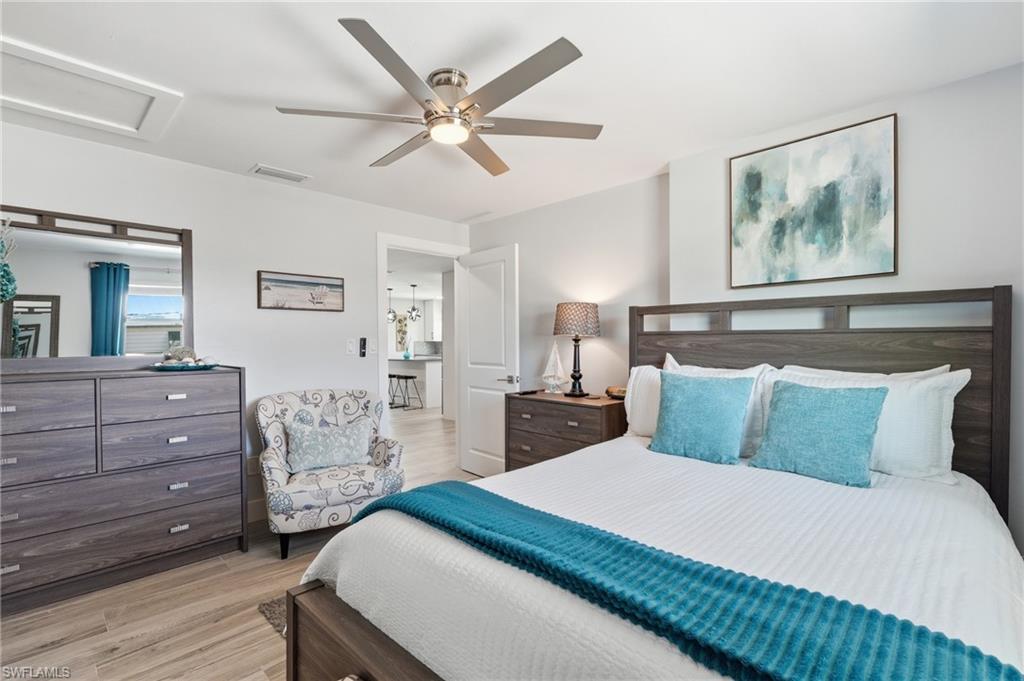 Spacious room featuring wood-finish flooring, a ceiling fan with integrated lighting, and a white paneled door - Virtually Edited Image