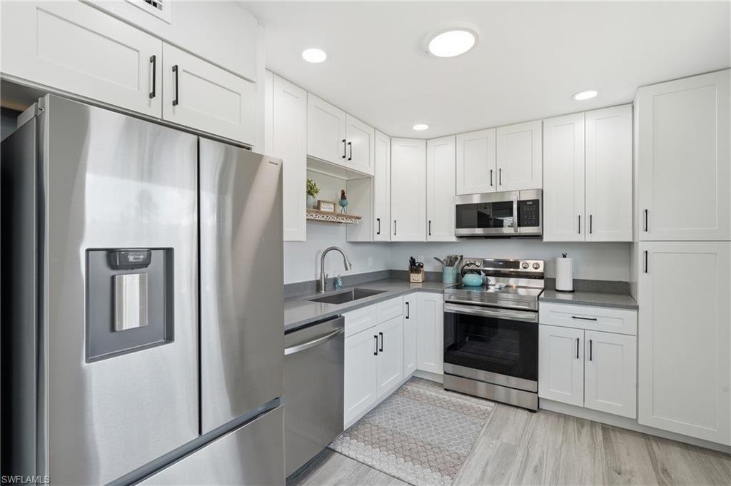 Modern kitchen featuring white shaker cabinetry with matte black hardware, stainless steel appliances, gray countertops, and wood-finish flooring - Virtually Edited Image