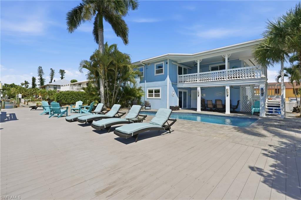 Expansive outdoor living area featuring a ground-level pool, an upper-level balcony with white railing, and a spacious deck - Virtually Edited Image