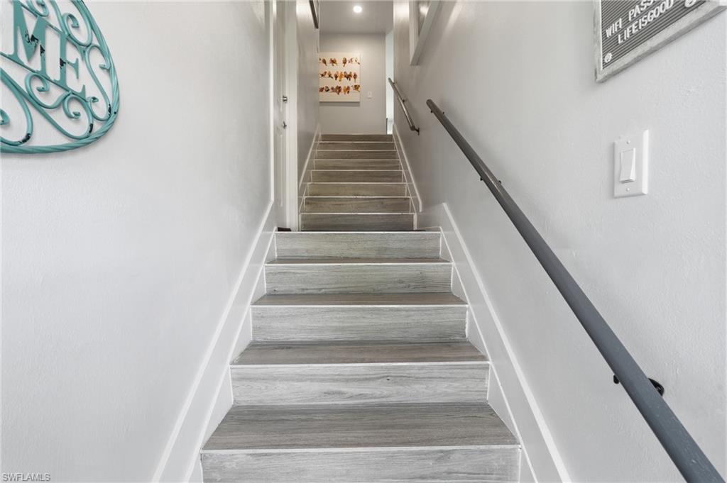 Staircase featuring wood-finish treads, a contrasting white riser, and a dark metal handrail - Virtually Edited Image