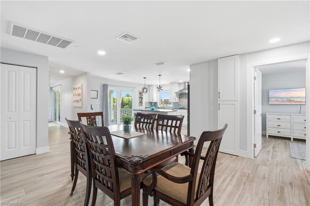 Open-concept living area featuring wood-finish flooring, recessed lighting, white bifold doors, and built-in white cabinetry - Virtually Edited Image