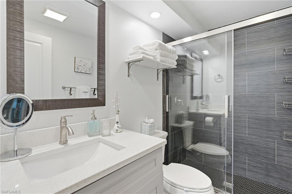 Bathroom featuring a frameless glass shower enclosure with gray horizontally tiled walls and a dark mosaic tile floor - Virtually Edited Image