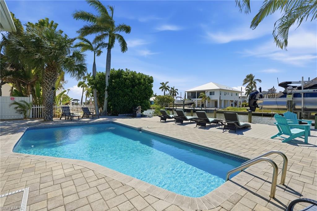 Rectangular swimming pool surrounded by a paver patio, featuring mature palm trees and direct water frontage - Virtually Edited Image