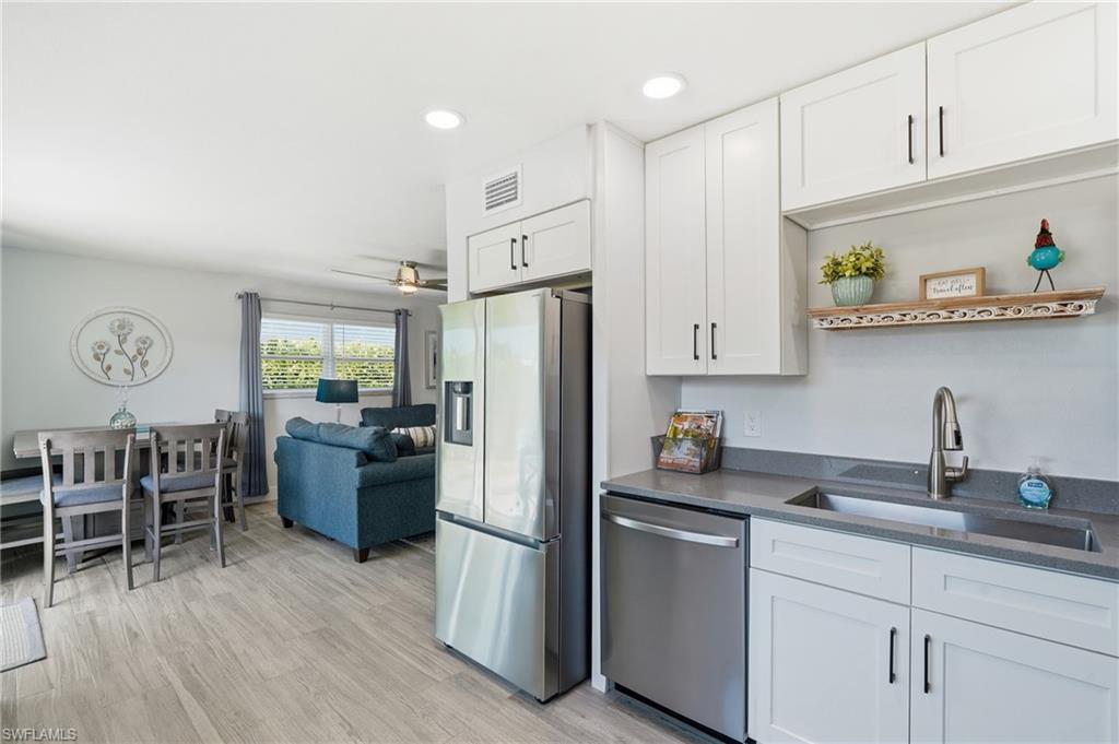 Open concept living area featuring contemporary white cabinetry, stainless steel appliances, stone countertops, and wood-finish flooring - Virtually Edited Image