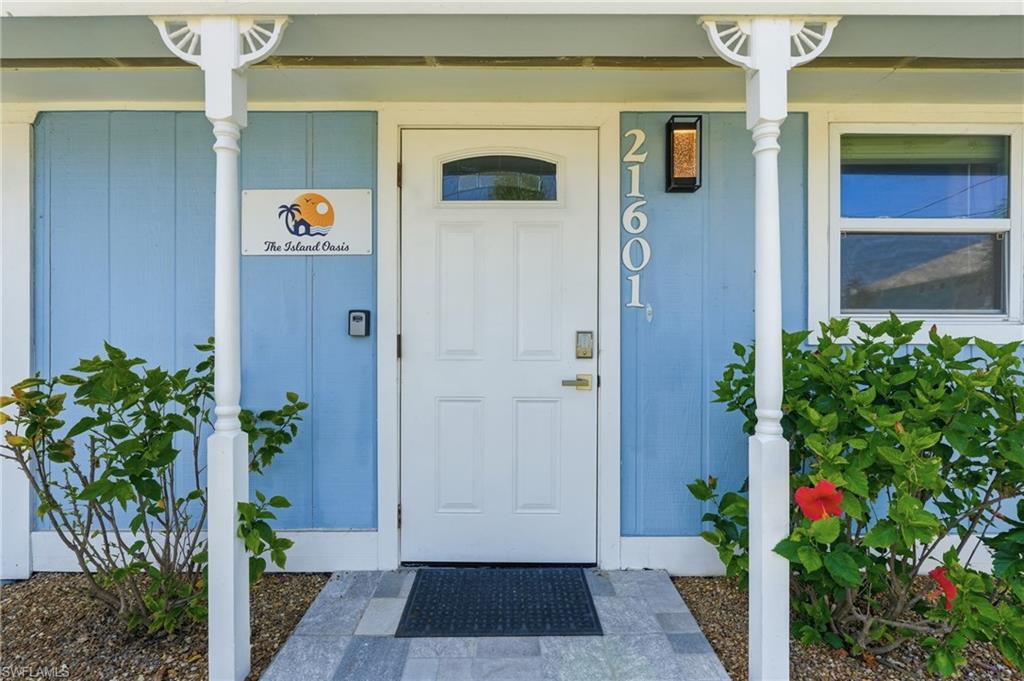 Entryway featuring a paneled door with an arched window, light blue siding, and white architectural columns - Virtually Edited Image